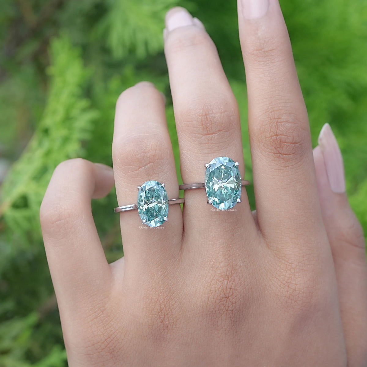 Front View of A Blue Green Oval Moissanite Solitaire Ring in two fingers