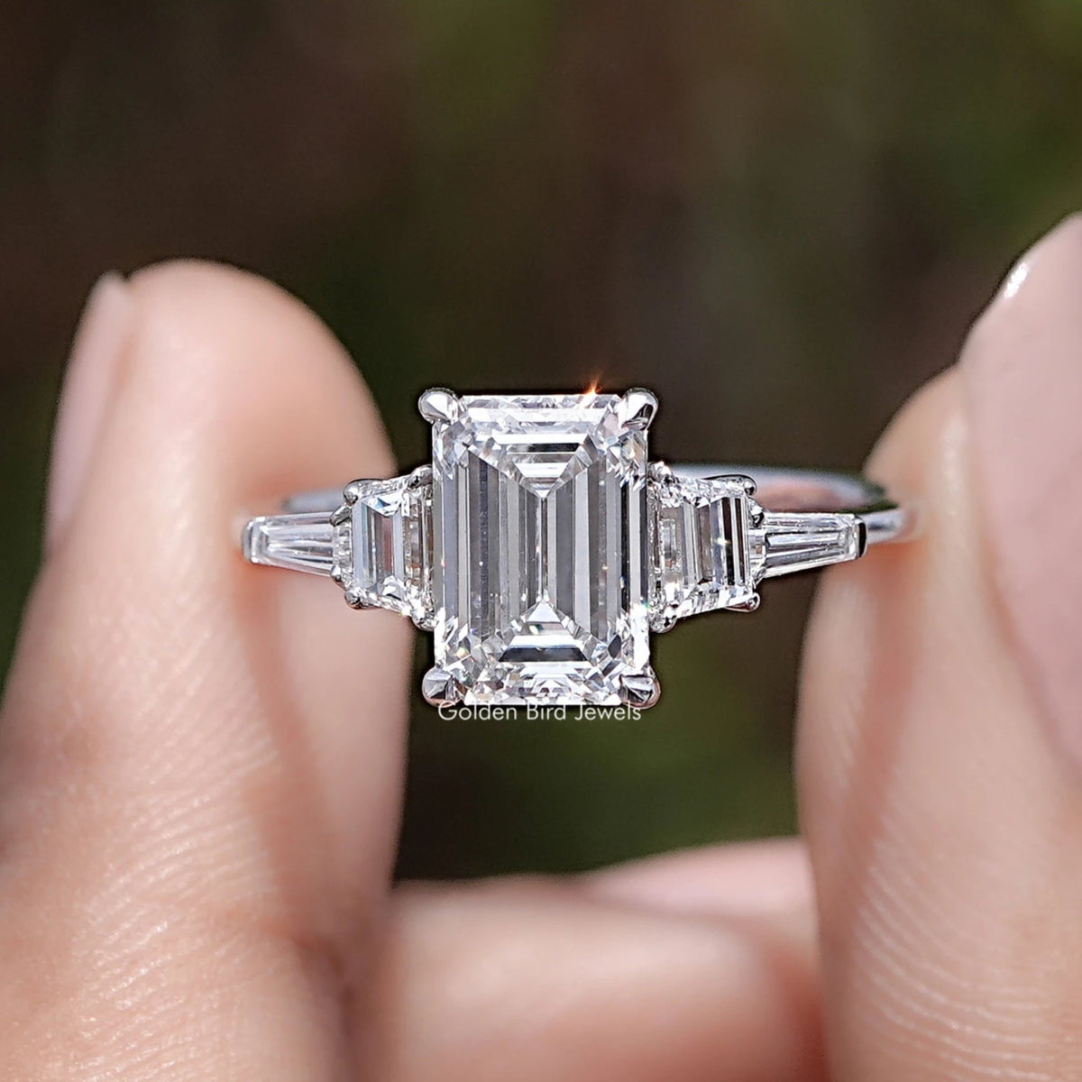 Emerald And Tapered Baguette Lab Diamond Ring Between Two Fingers