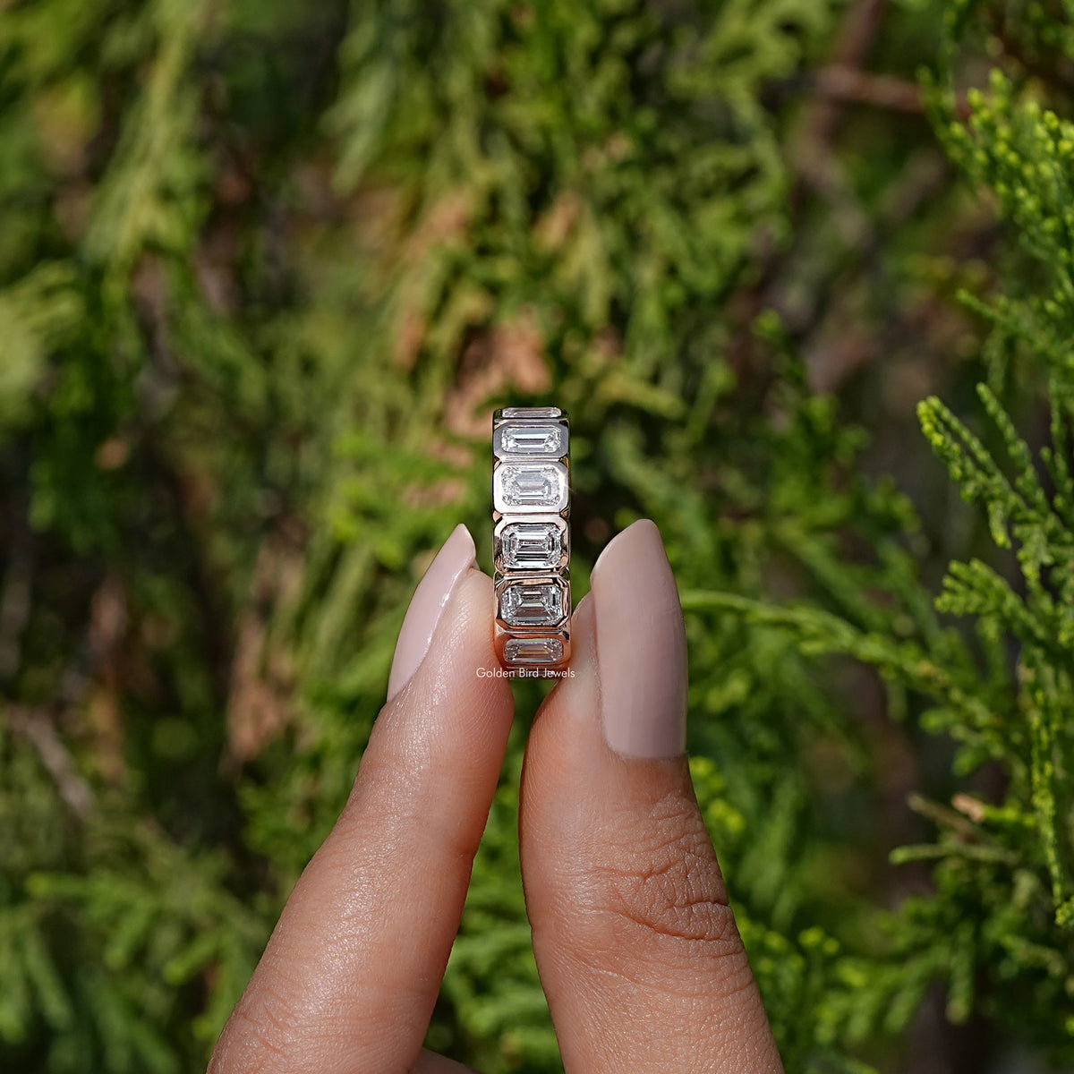 Side View of Emerald Cut Diamond Bezel Set Wedding Band In two fingers