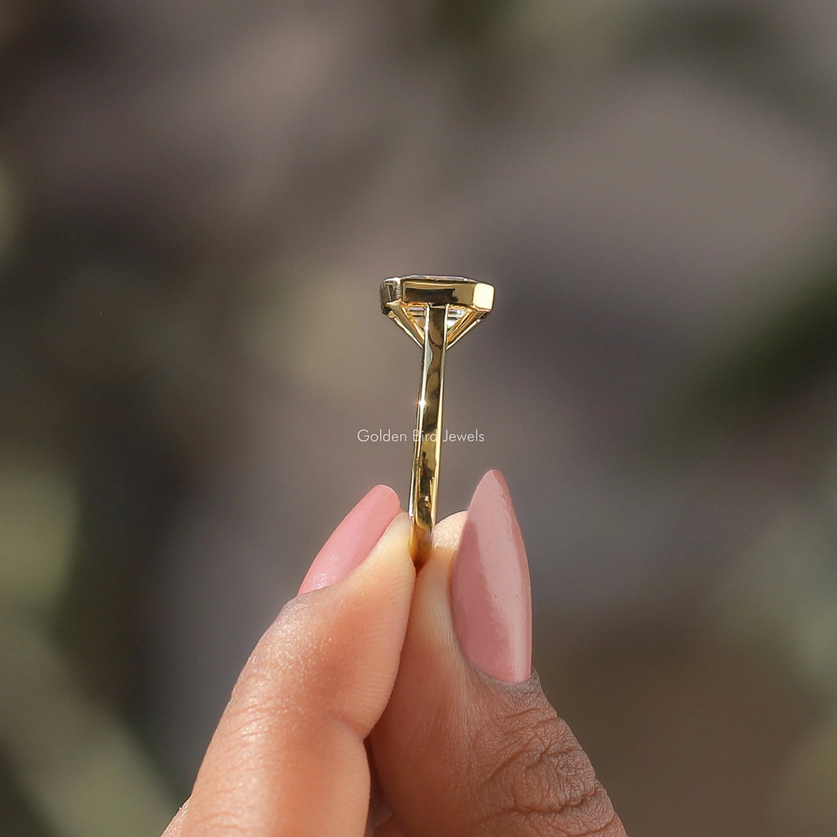 Side View of Emerald Cut Moissanite Bezel Set Ring In two fingers