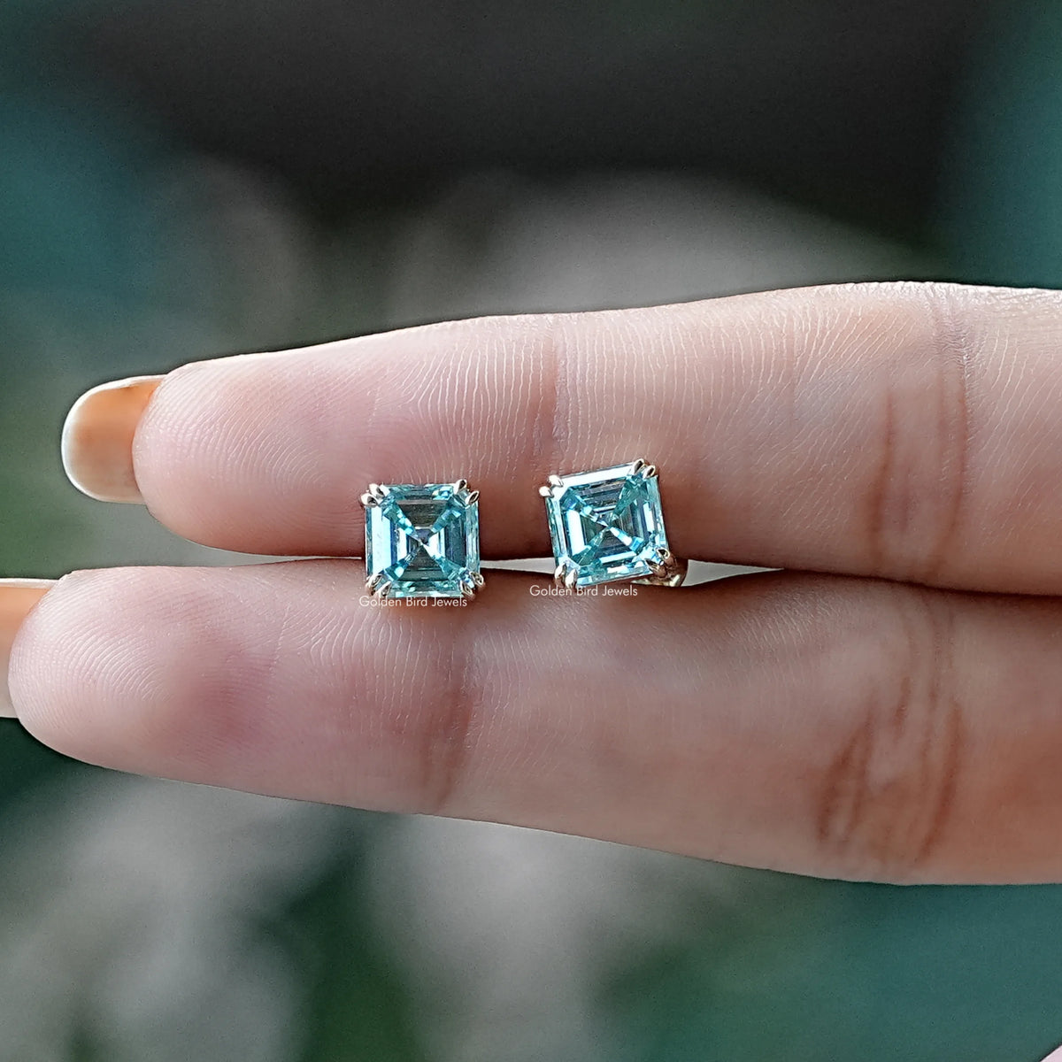 In two finger view of asscher cut moissanite stud earrings
