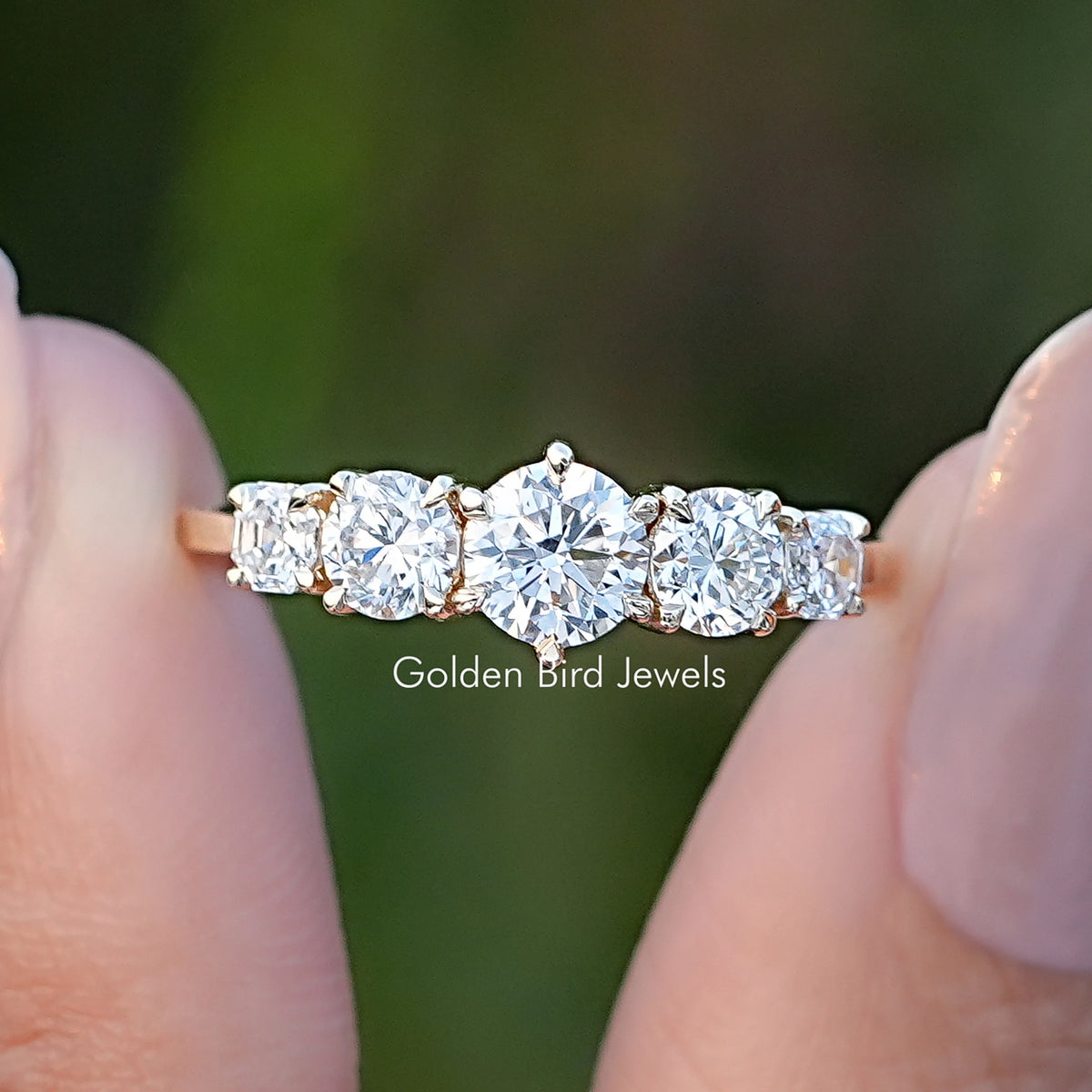 Octagon And Round Cut Lab Diamond Five Stone Ring Held Between Fingers