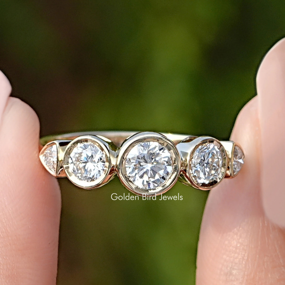 Round Cut Lab Diamond Five Stone Bezel Set Ring Held Between Fingers