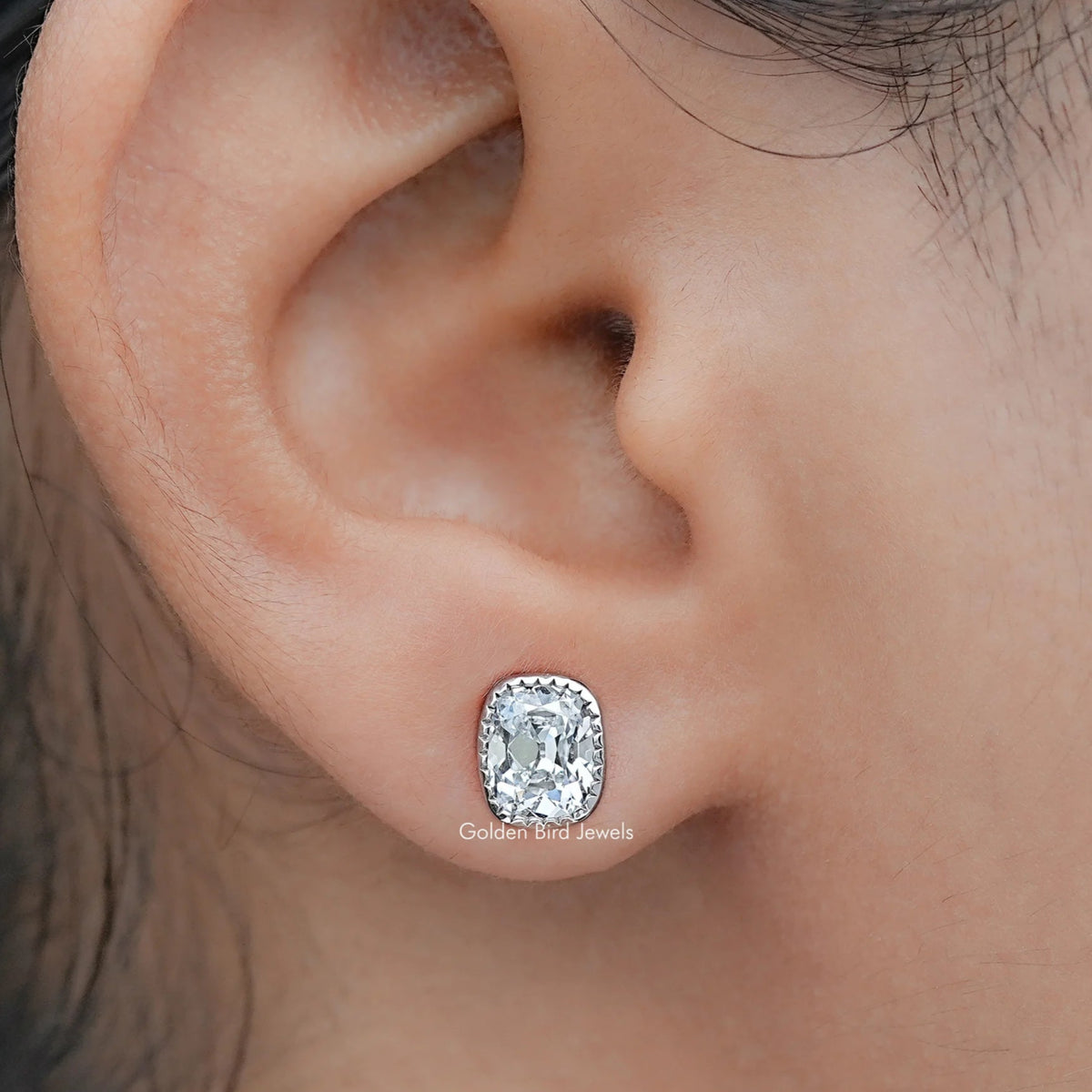 Close-up of an ear wearing a diamond stud earring with a blurred background