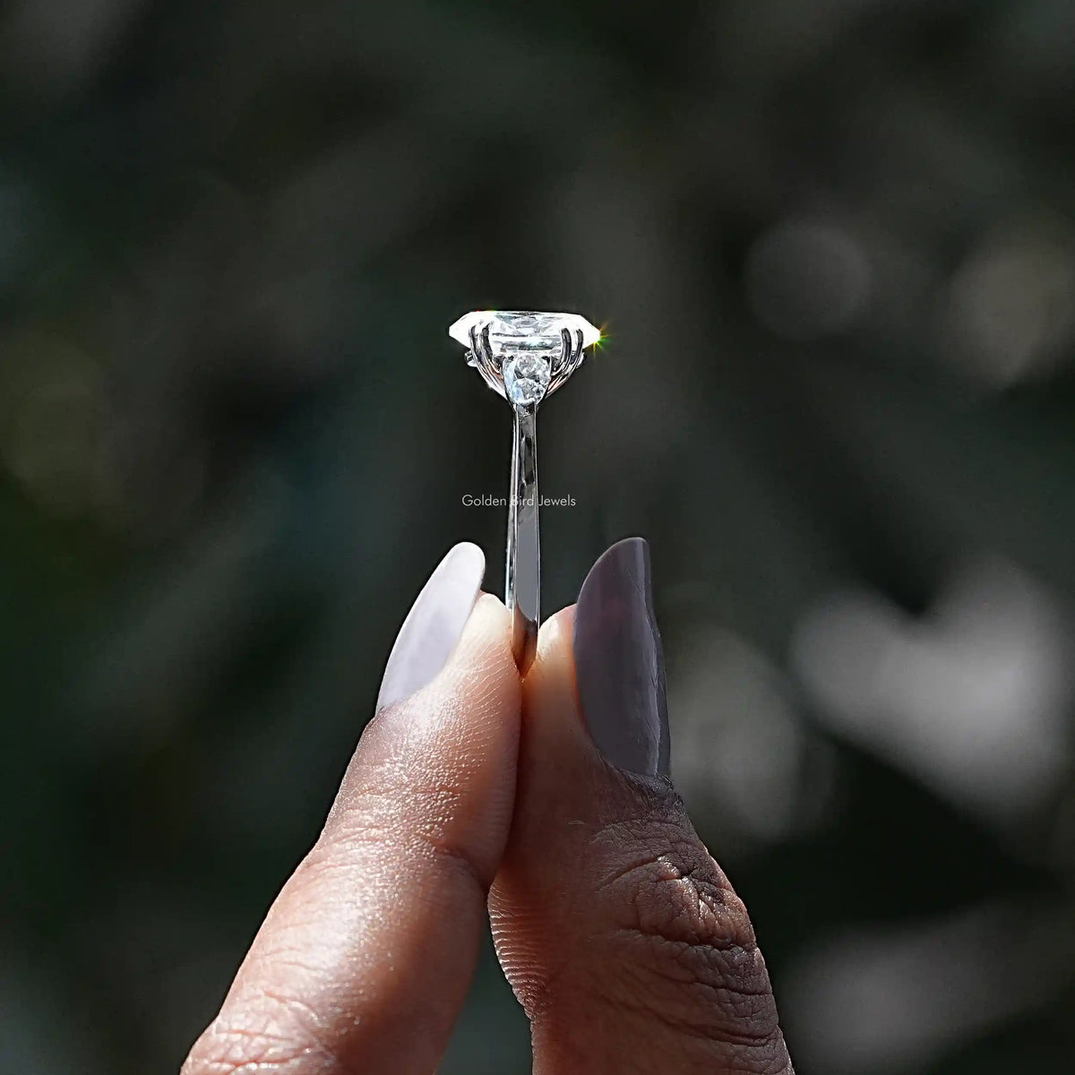 Side View of Oval And Pear Moissanite Three Stone Engagement Ring In two fingers