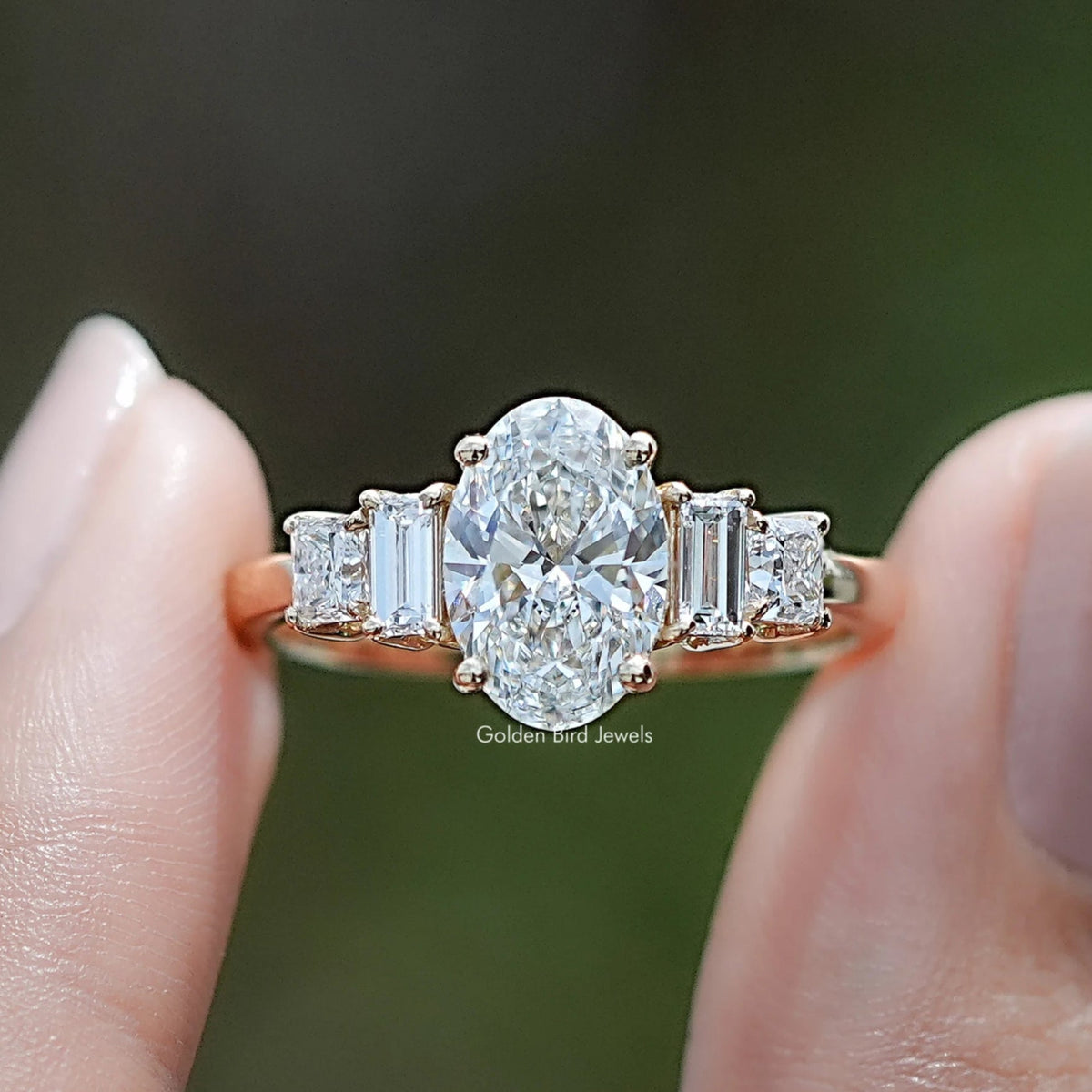 Oval Cut Lab Diamond Five Stone Engagement Ring BetweenTwo Fingers