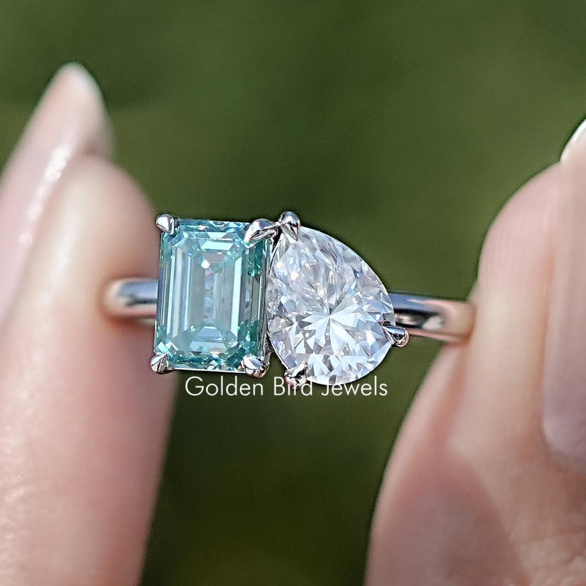 Front view of Pear And Emerald Cut Two Stone Moissanite Ring in two fingers