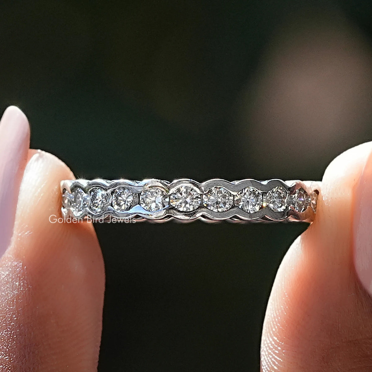 Bezel Set Round Diamond Wedding Band Held Between Fingers