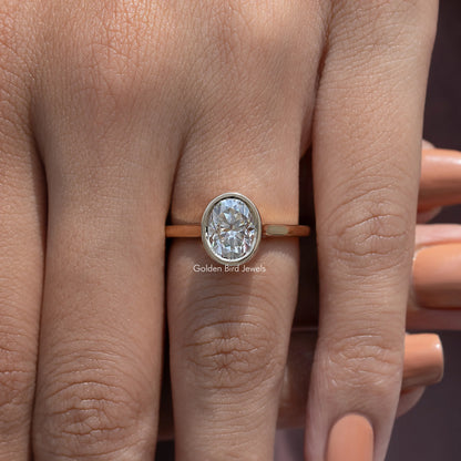 Oval moissanite solitaire ring on finger, bezel-set oval stone with slim gold band