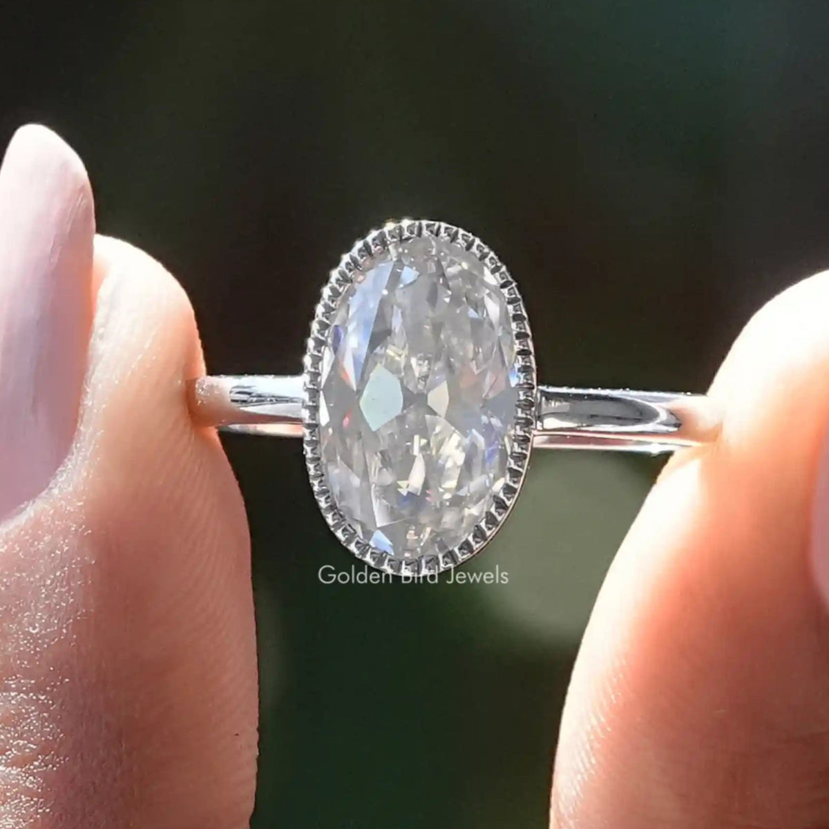 Two fingers holding the Oval Cut Bezel Set Moissanite Engagement Ring