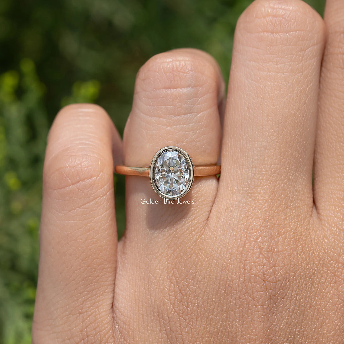 Oval moissanite solitaire ring on finger, bezel-set oval stone with narrow gold band