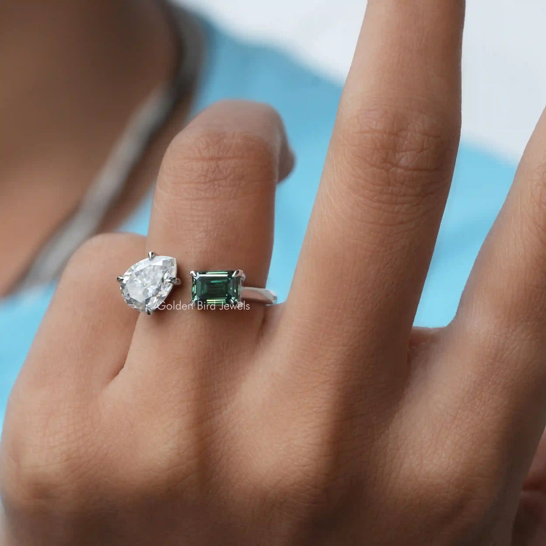 In finger front view of an emerald cut and pear-shaped Moissanite  ring 