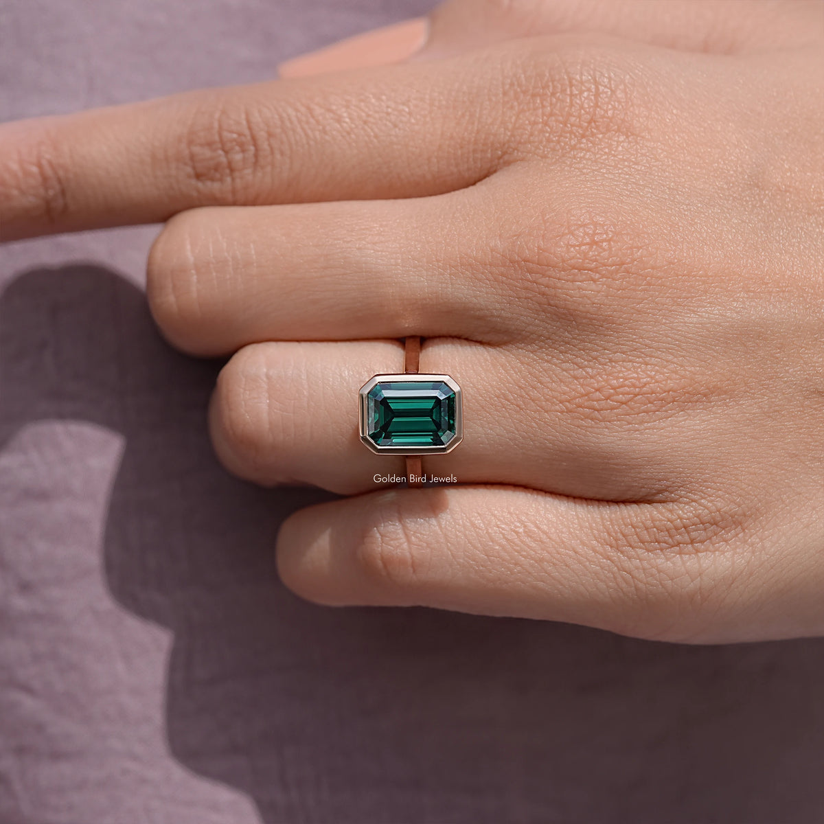 Emerald green moissanite solitaire ring close-up, rose gold-tone setting on palm