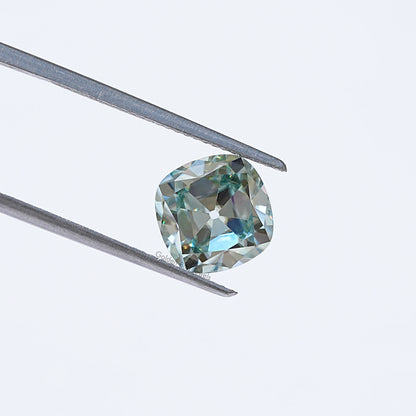 Light blue moissanite gemstone in silver tweezers, cushion old mine cut