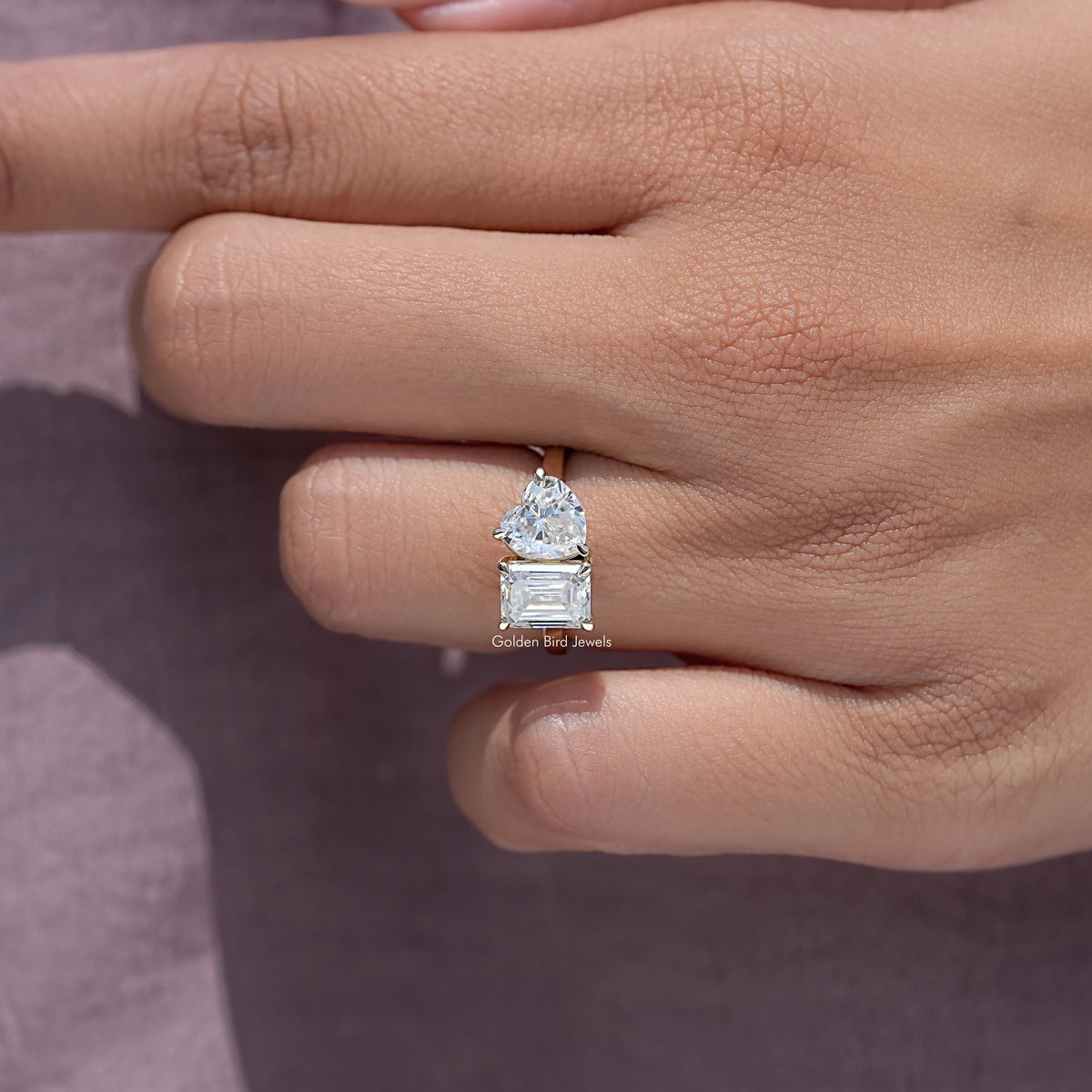 Toi et moi ring on finger, featuring emerald-cut and heart-shaped moissanite stones.