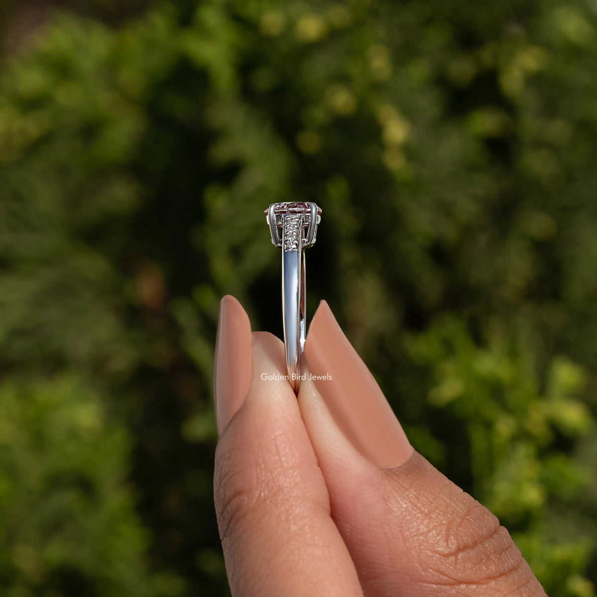 Silver ring with a diamond held between fingers against a blurred green background