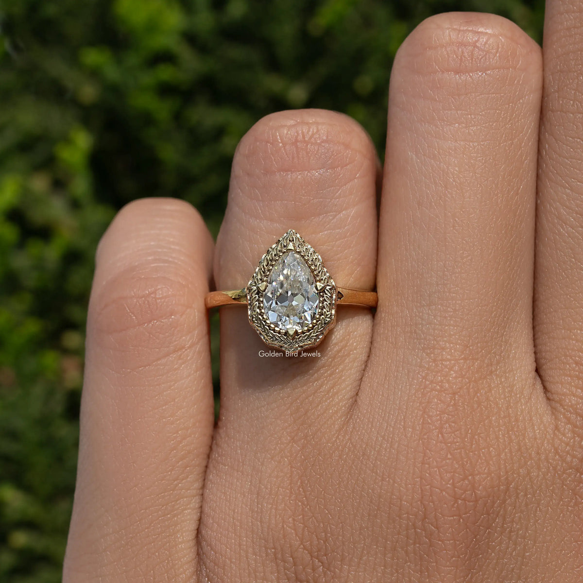 Pear-shaped moissanite solitaire ring on hand, gold-tone band with halo setting