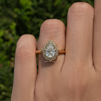 Pear-shaped moissanite solitaire ring on hand, gold-tone band with halo setting