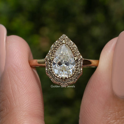 Pear-shaped moissanite solitaire ring with ornate halo and slim gold-tone band