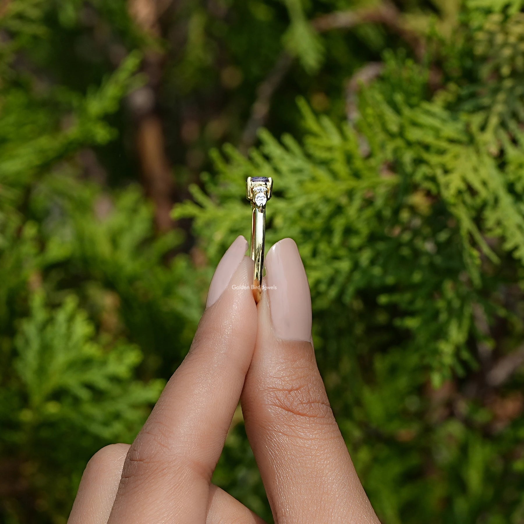 Side View of Round Cut Gemstone Accent Engagement Ring In two fingers