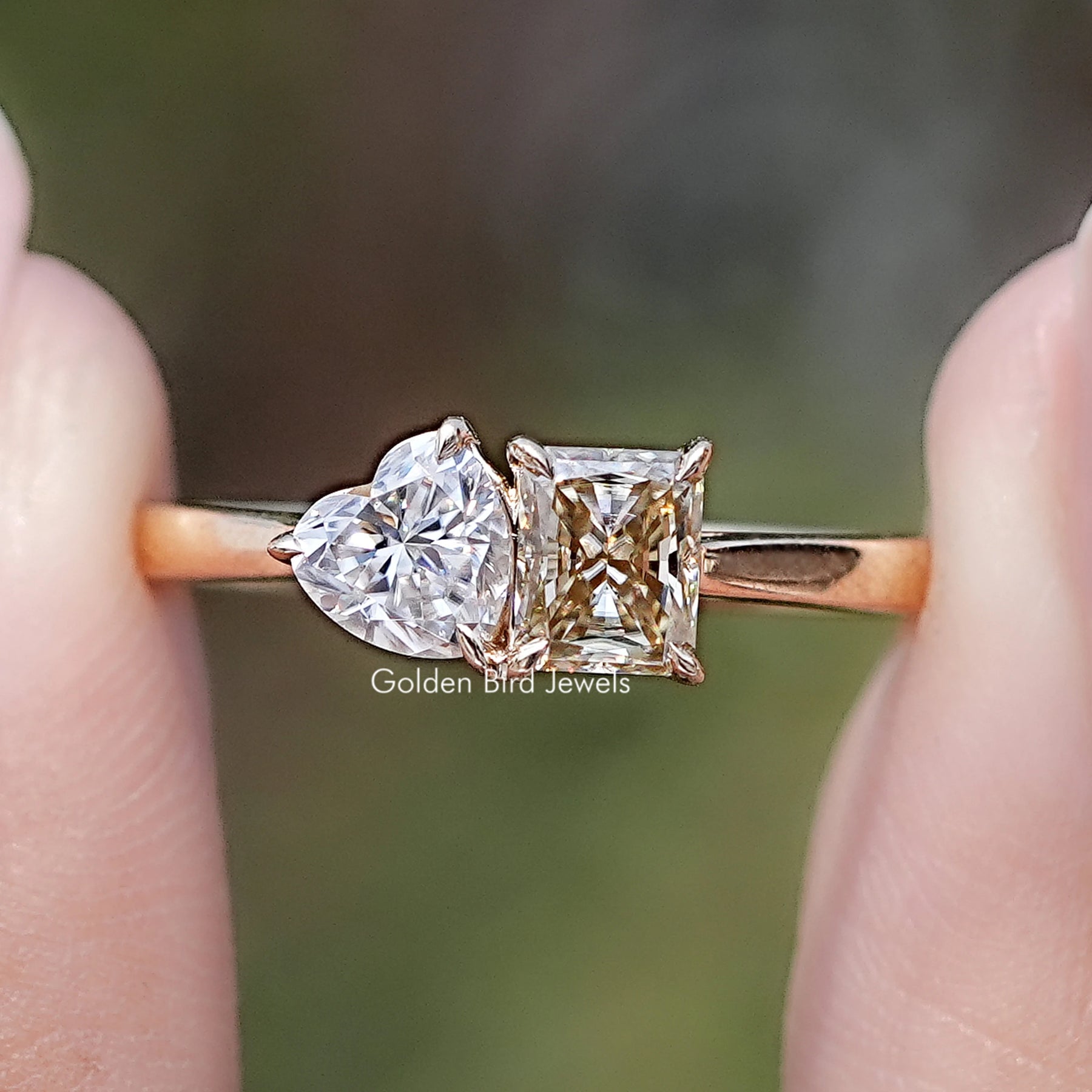 Front view of Radiant And Heart Cut Moissanite Two Stone Ring in two fingers 
