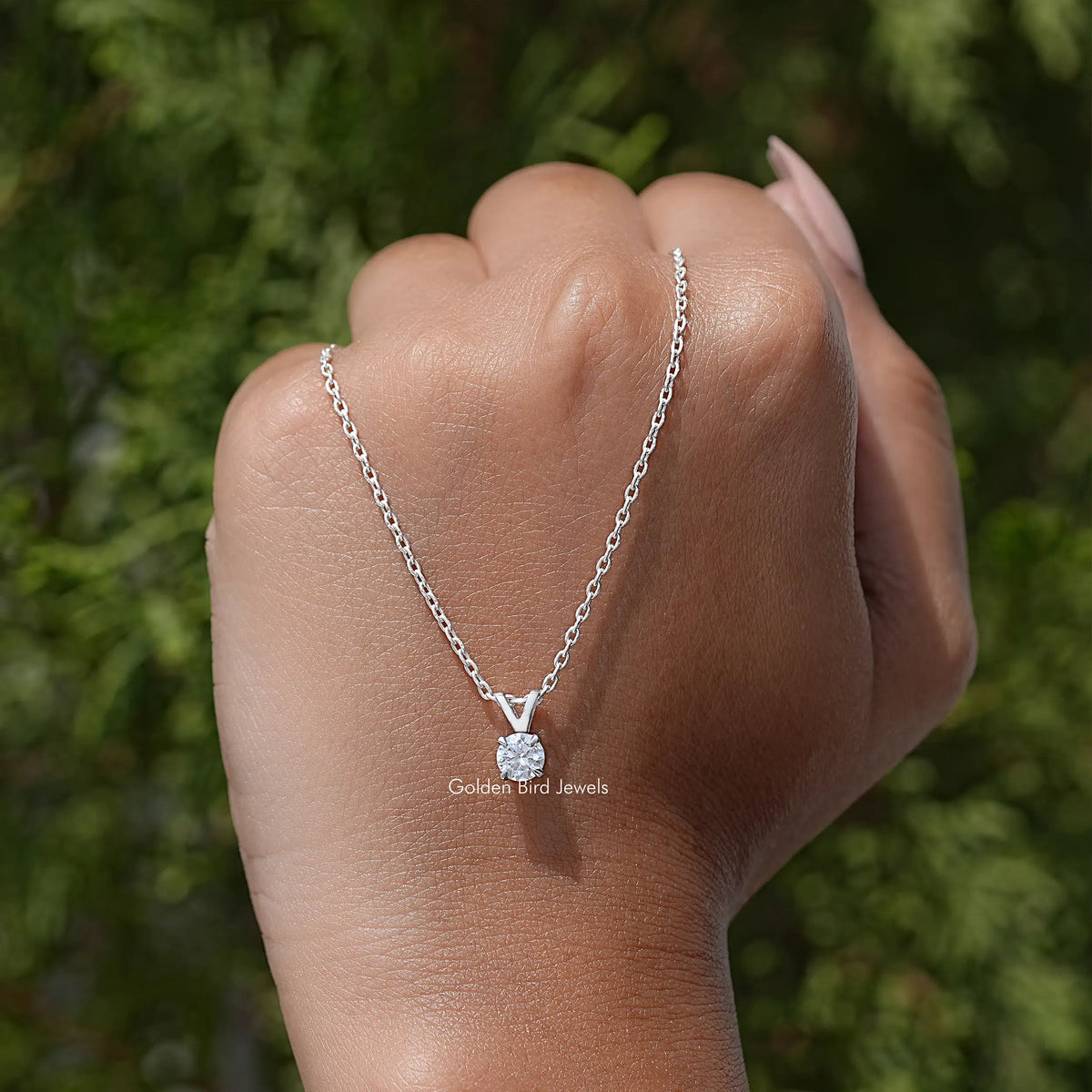 Silver round moissanite solitaire pendant on chain, worn on hand outdoors