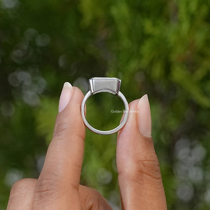 Sterling silver solitaire ring shown from the side, with a raised bezel-set emerald-cut stone