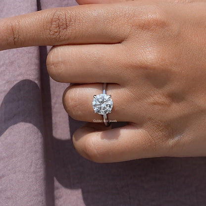 Round solitaire engagement ring on hand, featuring a prong-set round moissanite center stone